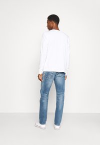 Langemouwen witte T-shirt en blauwe spijkerbroek. Het T-shirt heeft een ronde hals, en de spijkerbroek heeft vervaagd denim met achterzakken en een slim fit.