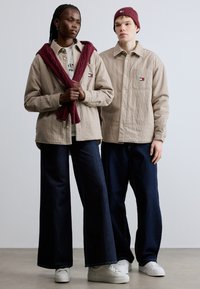 Bézs korddzseki ing, világosszürke ing, sötét farmer, bordó kötött sál és hozzá illő sapka. Fehér tornacipő teszi teljessé a megjelenést.