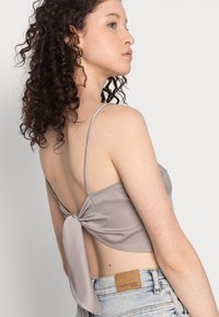 Top cropped cinza em cetim com alças finas e costas atadas, combinado com calções de ganga claros com um rótulo de patch em pele castanha.