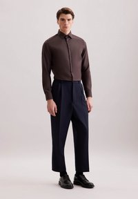 Bruine overhemdd blouse met lange mouwen, gecombineerd met hoog gesloten marineblauwe broek en zwarte veterschoenen. Eenvoudig ontwerp, gladde textuur.