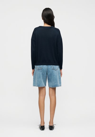 Μπλε σκούρο φούτερ με άνετη εφαρμογή και ριμπ μανσέτες, συνδυασμένο με ανοιχτό μπλε τζιν σορτς με φθαρμένο τελείωμα και πίσω τσέπες.