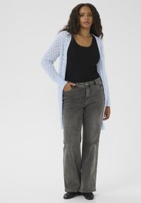Hellblauer, offener Strick-Cardigan über einem schwarzen Tanktop, kombiniert mit dunkelgrauen, weiten Jeans und schwarzen Schuhen.