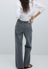 Weite Jeans aus verblasstem grauem Denim mit hoher Taille, zwei Gesäßtaschen mit Nahtdetails und einem hellbraunen Lederetikett.