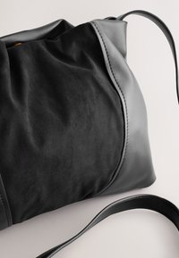 Must käekott, millel on seemisnahast tekstuur ja siledad nahast detailid. Sisaldab ühte reguleeritavat rihma. Struktureeritud, pehme siluett õmbluse detailiga.