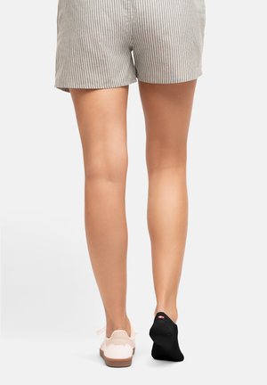 Hellrosa Sneakers mit strukturiertem Obermaterial und brauner Sohle, kombiniert mit einer schwarzen Kniesocke. Gestreifte Shorts. Beine sind im Bild zentriert.