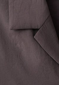 Tissu gris foncé avec des motifs floraux tissés subtils, montrant une section pliée mettant en valeur la texture et les détails du design.