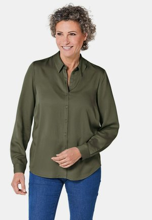 Donkergroen, langärmige knopshirts met een kraag, met een gladde textuur en een gebogen zoom, gecombineerd met blauwe jeans.
