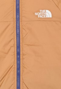 Hnědá bunda s modrým zipem a bílým logem The North Face na levém horním prsu.