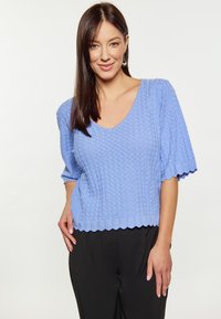 Helles blaues gestricktes Sweatshirt mit V-Ausschnitt, kurzen Ärmeln und gewelltem Saum. Der Stoff weist eine Rautenmusterstruktur auf.