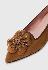 Brown pointed suede flat shoe with large flower decoration adorned with silver studs on the toe area and pink interior lining.