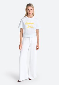White cotton t-shirt with "Lemon Juice" printed in yellow cursive, paired with wide-leg white trousers. Minimalist design, soft texture.