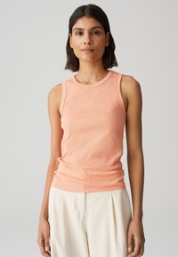 Top a manica corta color pesca con scollatura rotonda, design aderente e senza maniche, abbinato a pantaloni beige a gamba larga.