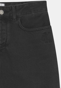 Mustat farkut, joissa on sileä pinta, etutasku, vyölenkit ja painettu brändin logo sivulla.