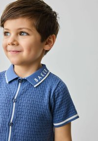 Plava polo majica kratkih rukava od teksturiranog materijala, s bijelim ovratnikom, plavim i bijelim prugastim detaljima te kopčanjem na dugmad. Ispod je izvezena riječ "BAKER".