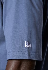 Modra bombažna majica s kratkimi rokavi in belim vezenim logotipom na levem rokavu. Gladka tekstura, čisti šivi na robu.