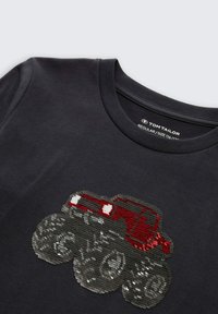 Schwarzes Baumwoll-T-Shirt mit einem Pailletten-Design eines roten Monstertrucks mit großen grauen Rädern und weißen Akzenten. Normale Passform, Rundhalsausschnitt.