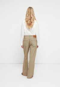 Μπεζ παντελόνι σε ίσια γραμμή με φθαρμένο μανίκι, διαθέτει δερμάτινη επιφάνεια στη μέση και πίσω τσέπες. Λείος υφασμάτινος χαρακτήρας, casual σχέδιο.