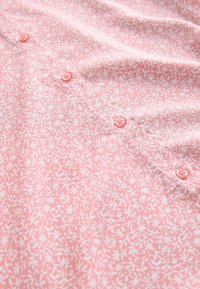 Rosa skjorta med ett blommigt vitt mönster och rosa knappar fram. Slät tyg med en lätt textur.