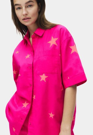 Camicia rosa a maniche corte con un motivo di stelle arancioni chiare, chiusura frontale con bottoni, colletto e una tasca sul petto. Texture morbida.