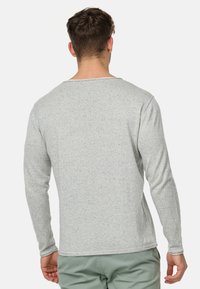 Jasnoszary, długi rękaw T-shirt z teksturowanej tkaniny, okrągłym dekoltem i płaskimi szwami. Widok z tyłu podkreśla swobodny krój i minimalistyczny design.