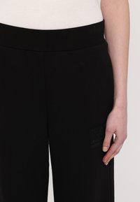 Čierne teplákové nohavice s jemnou textúrou, s širokým pásom a obdĺžnikovou nášivkou s nápisom "EA7 EMPORIO ARMANI" v decentnom embosovanom prevedení.