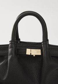 Borsa a mano nera in pelle con finitura texturizzata, doppio manico e dettagli in metallo dorato sulla parte anteriore. Design elegante e pratico.