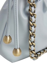 Svetlo modra usnjena torbica s zlatim verižnim ročajem in dvema dekorativnima kovinskima dodatkoma z vgraviranim besedilom na koncih.