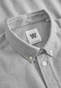 Camisa de color gris con cuello de textura. Presenta un cuello abotonado y botones blancos. La etiqueta dice "DOUBLE V by WOOD WOOD", tamaño M.