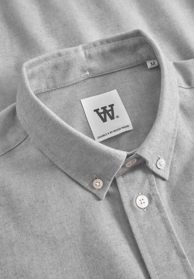 Chemise grise à col, fabriquée en tissu texturé. Présente un col boutonné et des boutons blancs. L'étiquette indique "DOUBLE V by WOOD WOOD", taille M.