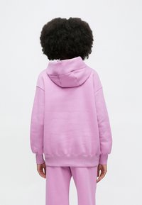 Overdimensjonert rosa hettegenser med snor i hetten og ribbestrikkede mansjetter. Myk tekstur og avslappet passform, kombinert med matchende bukser.