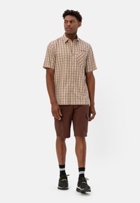 Korte mouwen geruite shirt in beige met bruine en oranje lijnen, gecombineerd met bruine cargoshorts. Zwarte sneakers met gele accenten maken de look compleet.