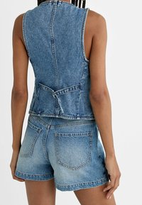 Denim ärmlös jacka med hög halsringning, justerbart knytband i midjan och fickor med lappar. Syra-tvättad effekt i ljusblå.