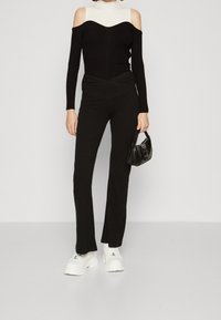 Top nero scivolato dalle spalle con texture a coste e design aderente, abbinato a pantaloni neri svasati e sneaker bianche con platform. Piccola borsa nera.