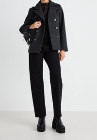 Chaqueta de lana mixta gris carbón de doble faz con grandes botones. Combinada con pantalones negros de talle alto y botas de plataforma negras gruesas.