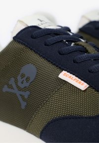 Marineblauwe en olijfgroene sneakers met een gestructureerde mesh bovenkant, suède accenten, een schedellogo en een oranje 'SCALPERS' label.