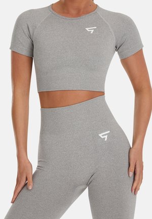 Femme portant un crop top gris clair assorti et des leggings taille haute sans coutures, avec de petits logos sportifs blancs sur la poitrine et la hanche.