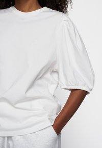 Biały bawełniany T-shirt z bufiastymi rękawami, prążkowanym dekoltem i luźnym krojem. Oversize'owy fason o gładkiej, miękkiej fakturze.