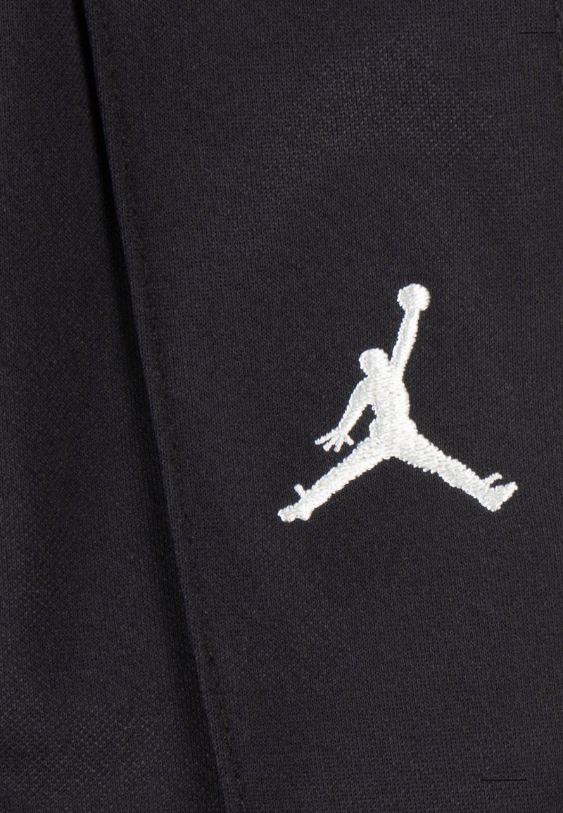 Tessuto nero con un grande logo Jumpman ricamato in bianco. La texture è liscia con una leggera lucentezza. Nessun altro motivo o accento presente.