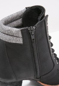 Stivaletto nero con pelle texturizzata, fodera a motivo a spina di pesce, zip laterale e lacci tondi. Presenta un tacco robusto per un buon supporto.