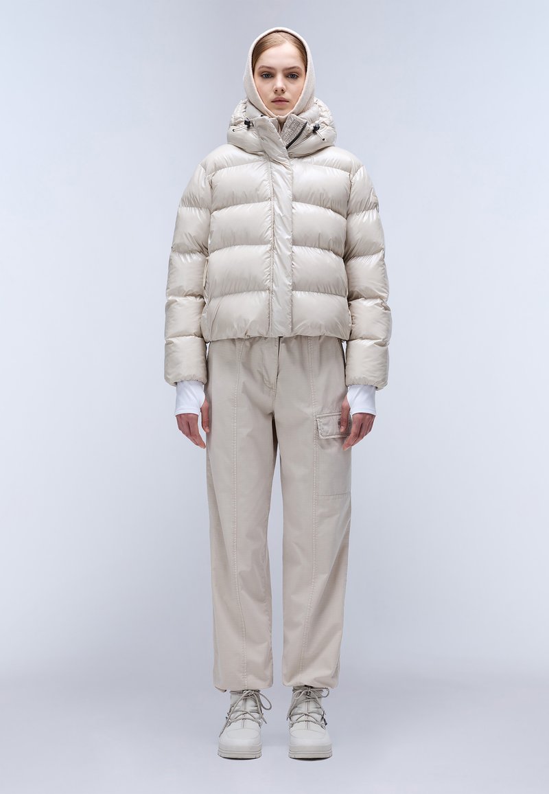 Giacca corta, leggera e imbottita di colore beige lucido, abbinata a pantaloni beige larghi con tasca laterale e sneakers bianche.