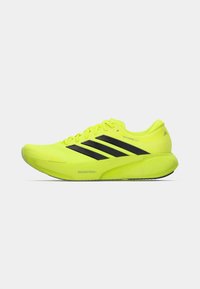 Φωτεινό κίτρινο αθλητικό παπούτσι με μαύρες ρίγες Adidas, παχύ πέλμα με την ετικέτα "DREAMSTRIKE+" και σήμανση "SUPERNOVA RISE 3".