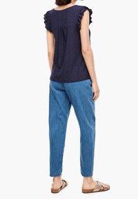 Haut bleu marine à manches courtes avec des détails à volants, tissu texturé, associé à un pantalon en jean bleu clair et des sandales marron à enfiler.