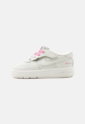 Zapatilla blanca de Nike con cordones rosas y detalles florales, con diseño de corte bajo y suela de goma gruesa.