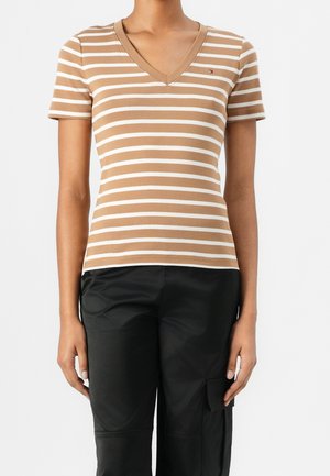 Maglietta a righe marroni e bianche con scollo a V, realizzata in morbido tessuto misto cotone. Design aderente con maniche corte, abbinata a pantaloni neri.