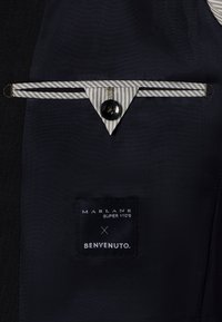 Detail eines navyblauen Anzugs aus Stoff mit gestreiftem Taschenbesatz, schwarzem Knopf und einem Etikett mit "MARLANE SUPER 110'S X BENVENUTO."
