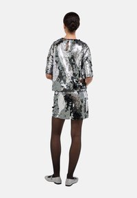 Ensemble deux pièces en sequins argentés comprenant un haut à manches courtes et une mini-jupe ; texture brillante avec des accents réfléchissants. Porté avec des collants noirs transparents.