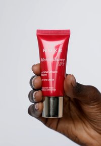 Tubo rojo con base plateada, etiquetado "NUXE Merveillance LIFT," para crema de ojos. Presenta una parte superior estriada, textura suave y texto en negrita.
