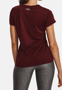 Maronrød atletisk t-shirt med korte ærmer, med en lille logo på øvre ryg. Stoffet ser glat ud med lidt stretch.