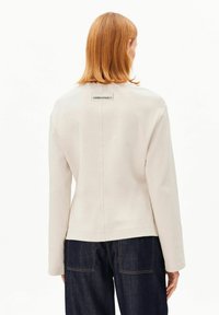 Beiger Pullover mit lockerem Schnitt, ausgestattet mit einem quadratischen Etikett auf der Rückseite. Weiche Textur, lange Ärmel und eine klare Silhouette.