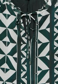 Blusa verde e bianca con motivo geometrico, colletto con laccio e finitura in tessuto testurizzato.